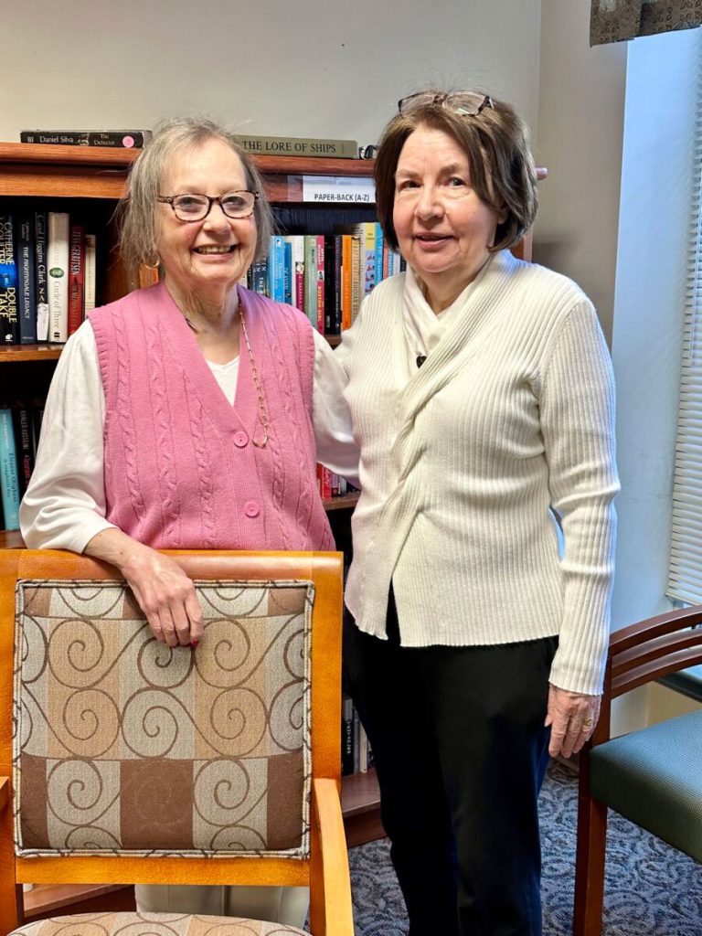 two women staning by chair