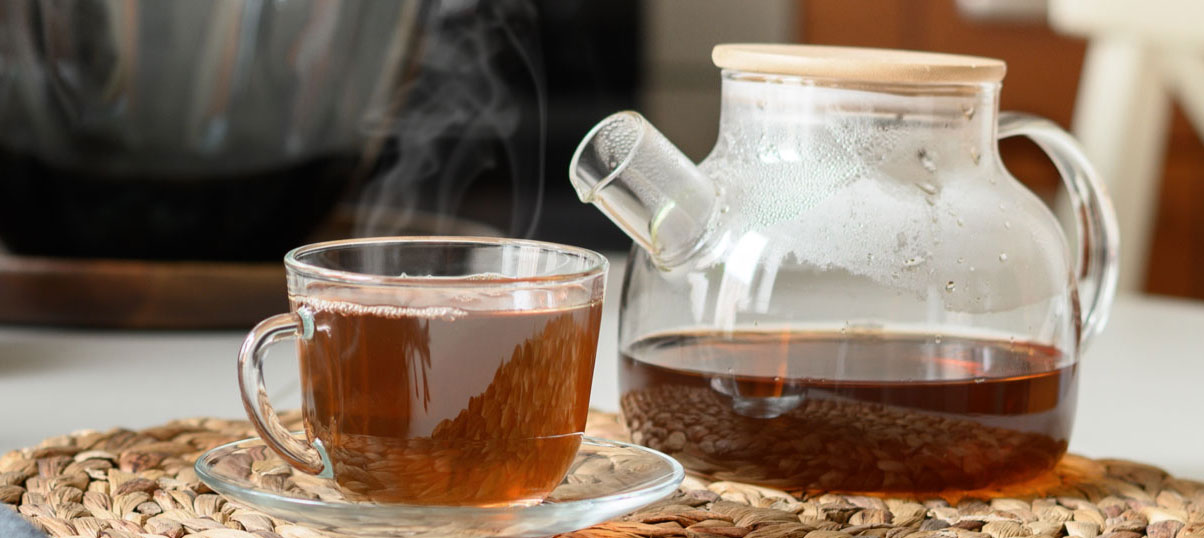 Close up of a glass tea pot and cup of tea.