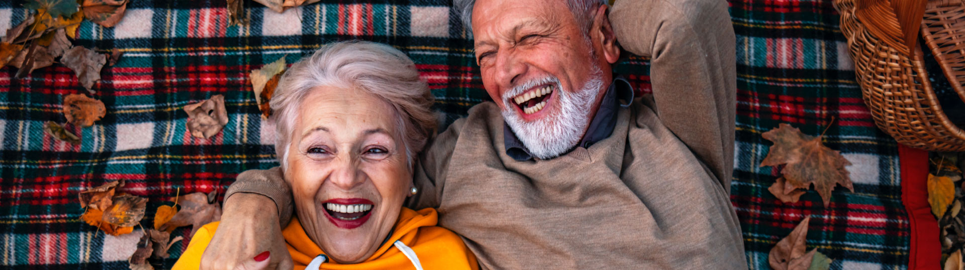 A senior couple laying on a plaid flannel blanket on a fall day.