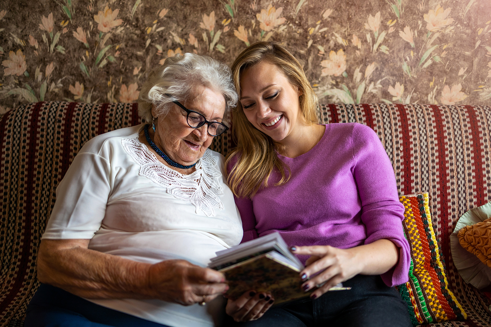 An elderly woman and her adult daughter look at a photo book together
