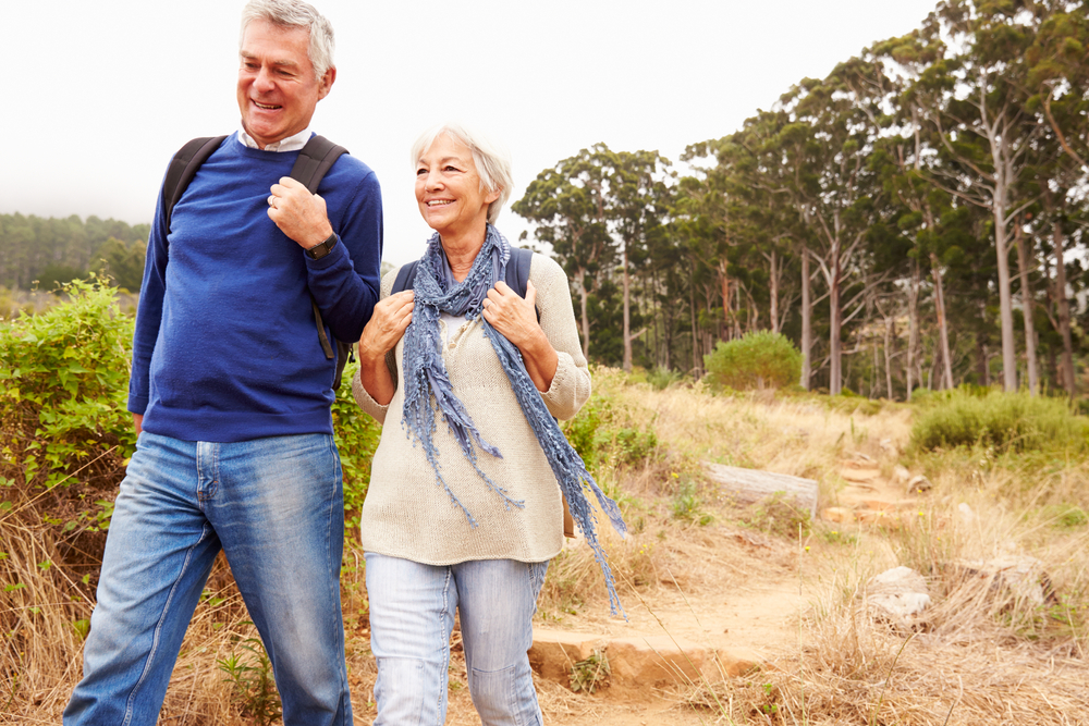 A senior couple hike with backpacks on along a trail.