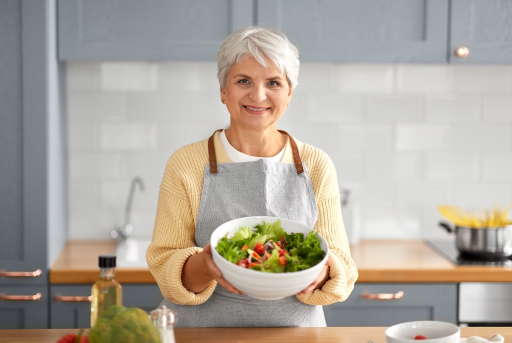 A senior woman holds up a large, colorful bowl of salad.