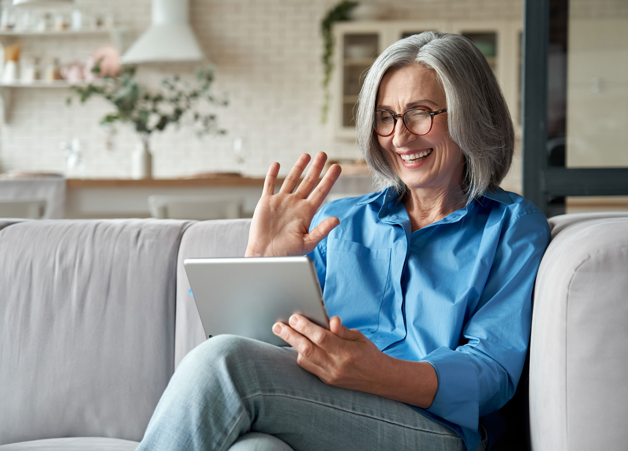 A senior woman laughs and waves while video chatting on a tablet.