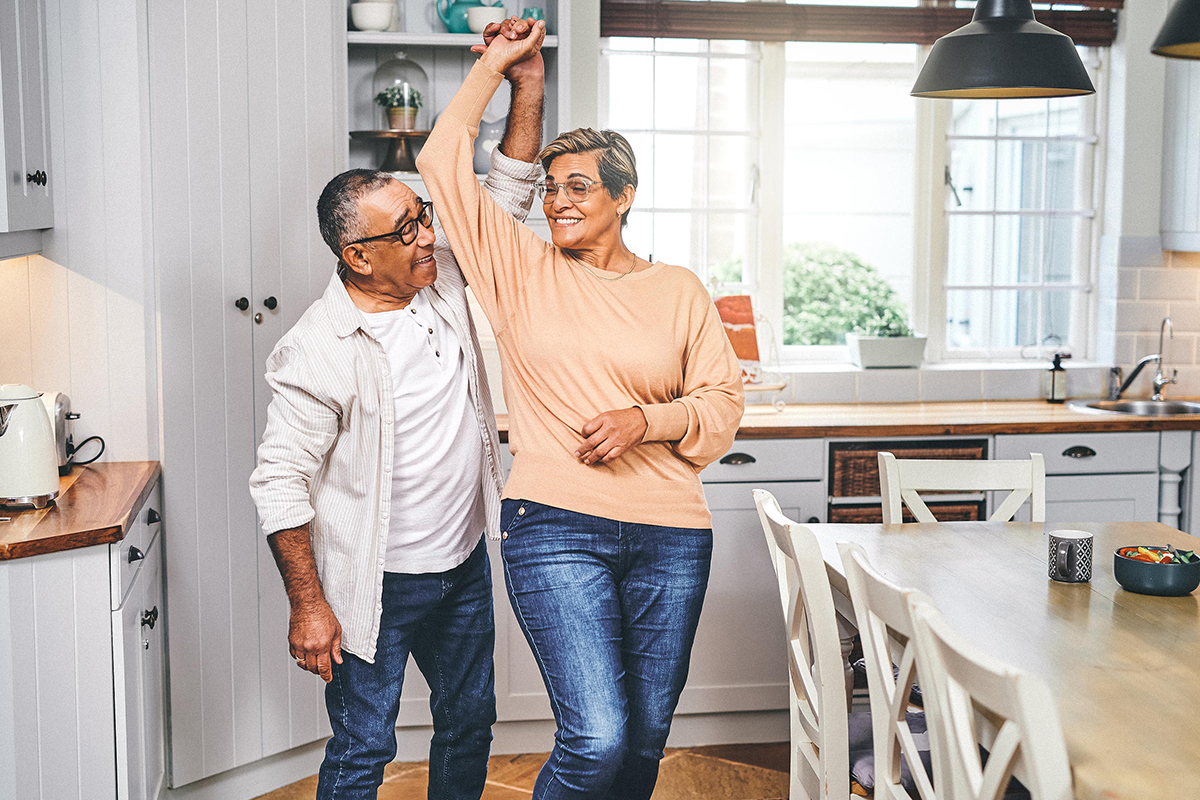 A senior couple dance together in the kitchen.