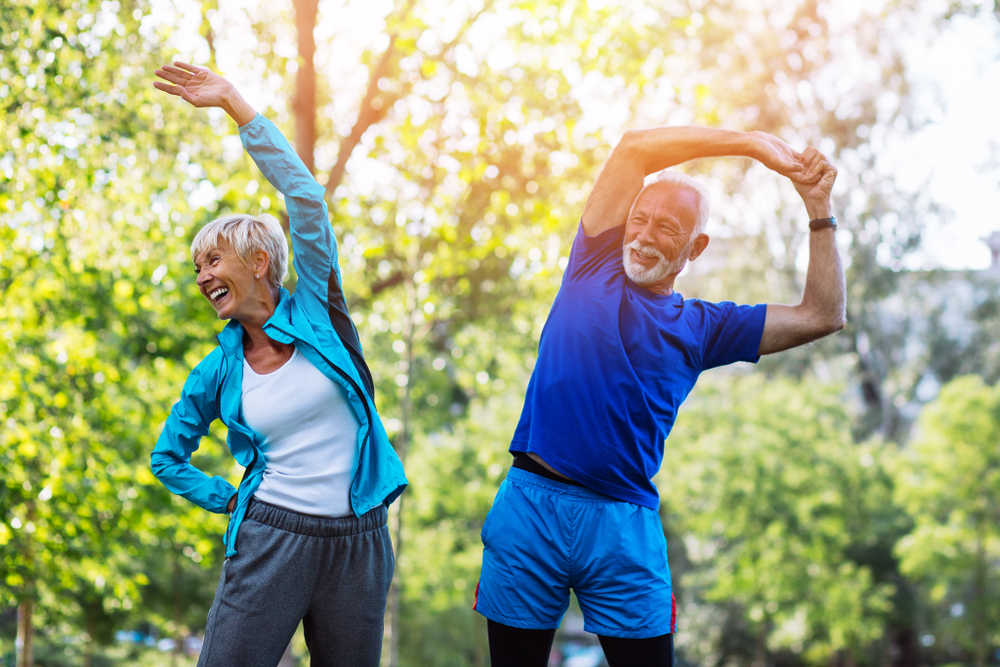 A senior couple stretch outside together.