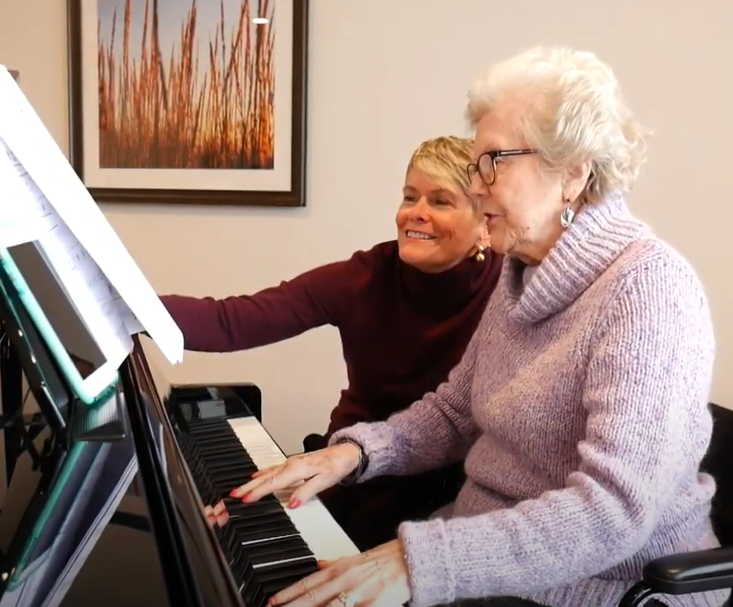 A senior woman sits with her daughter while playing the piano.