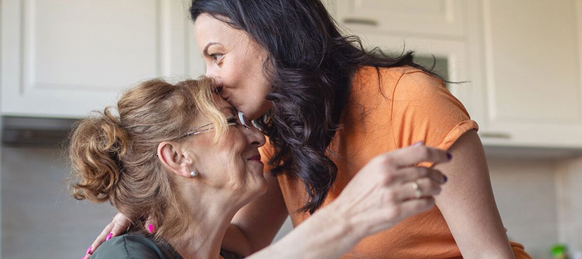 adult daughter kissing her elderly mother on the forehead