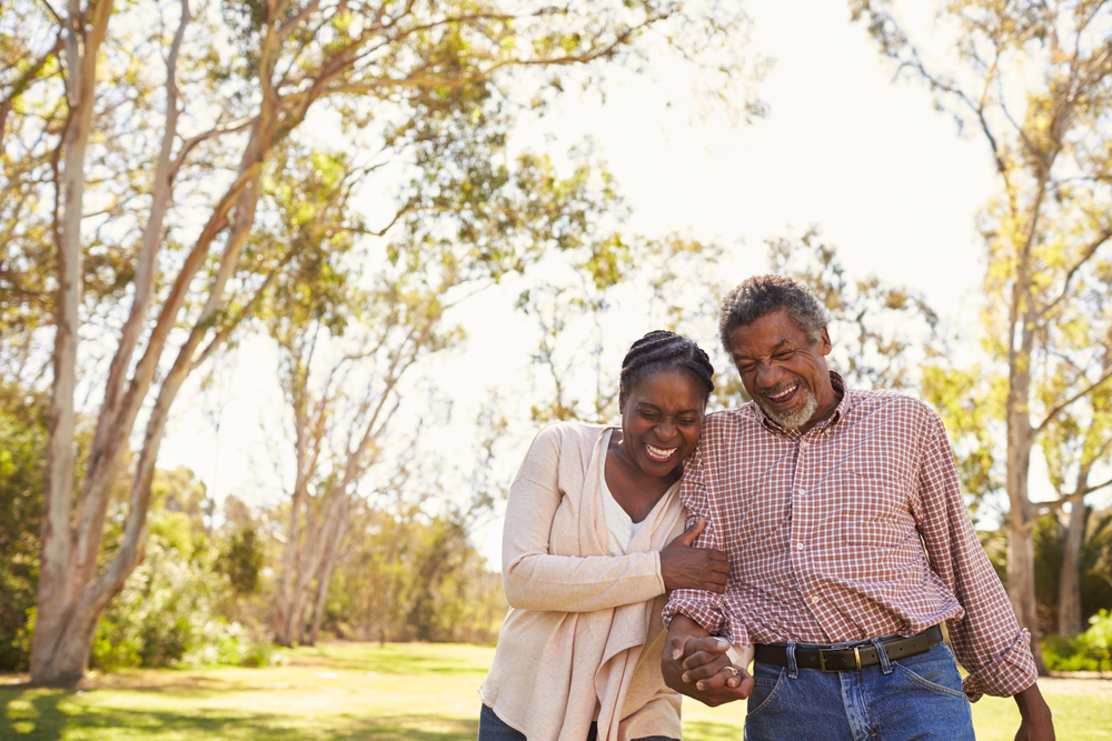 A senior man and woman smile and laugh while walking outside.