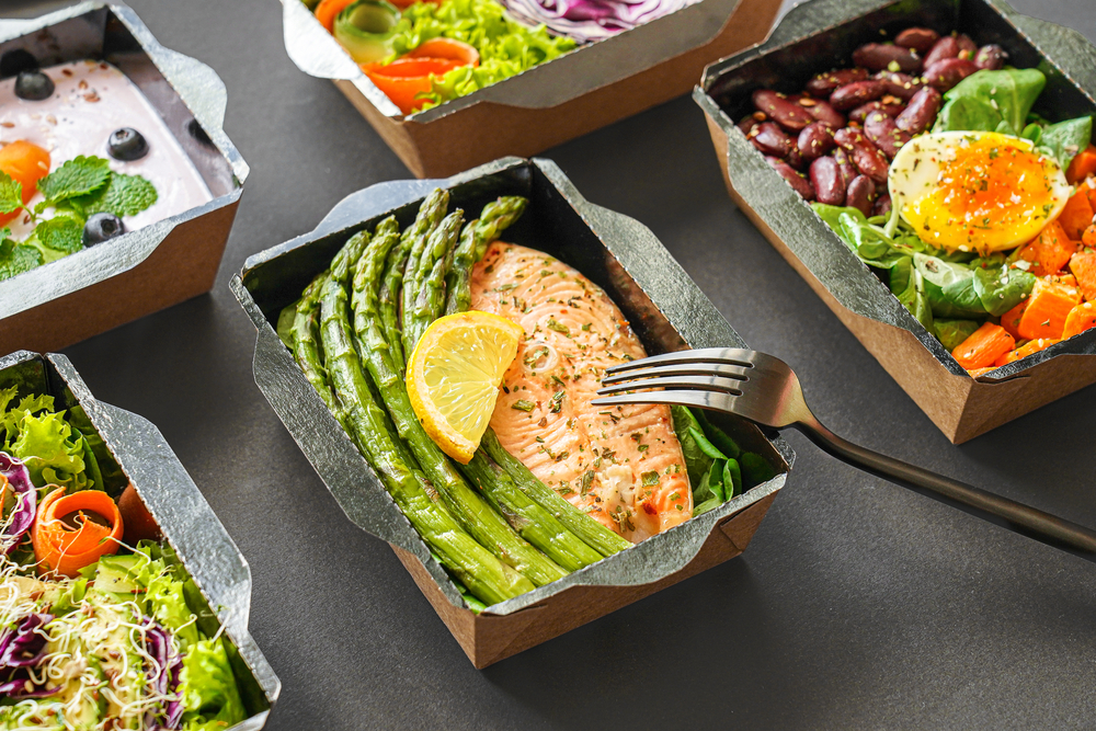 Close up of takeout containers with healthy meals displayed.