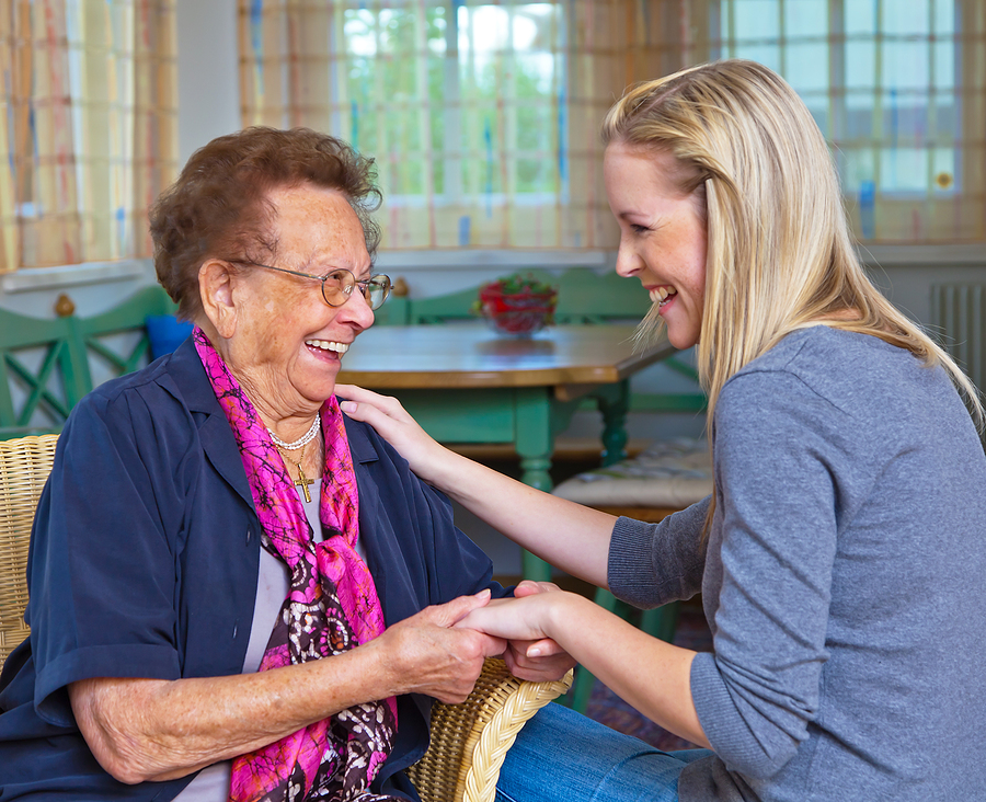 An elderly woman holds the hands of a young woman