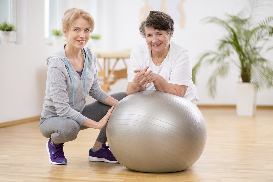 Two older woman exercise using a stability ball