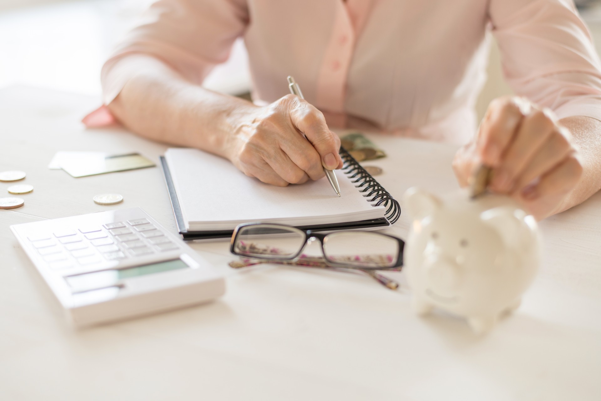 Close up of a senior woman's hands working with a calculator and writing notes down.