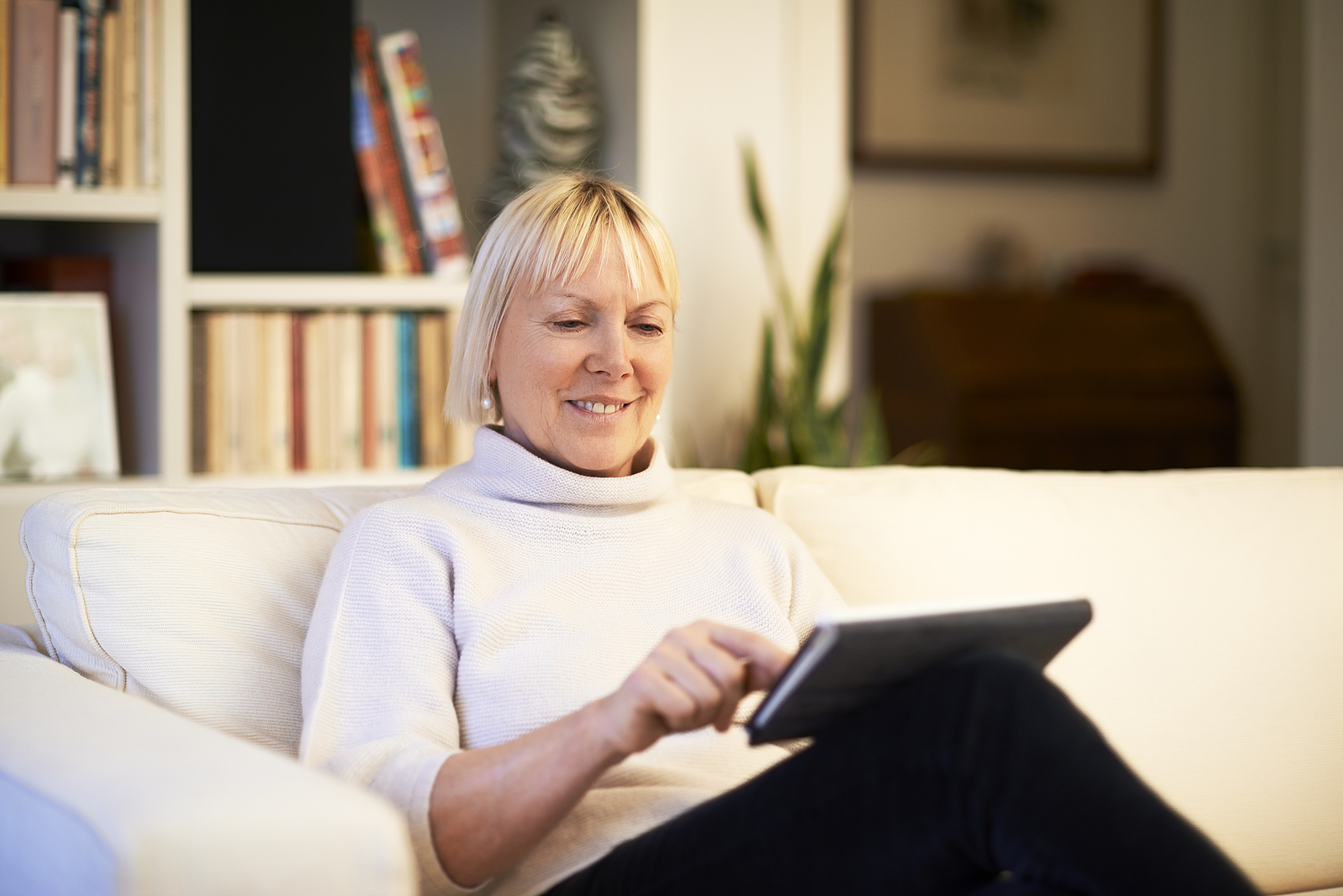 A woman sitting on her sofa, using a tablet.