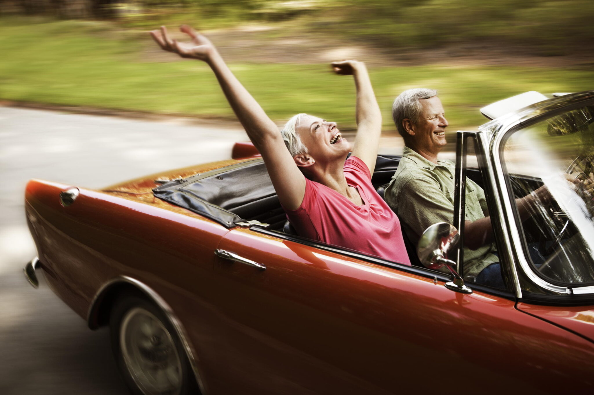 A senior couple going for a joy ride in a red convertible.
