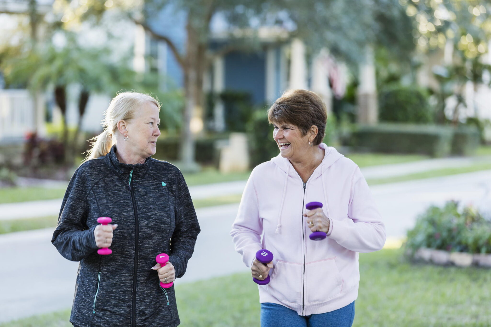 Two senior women walking with hand weights outside.