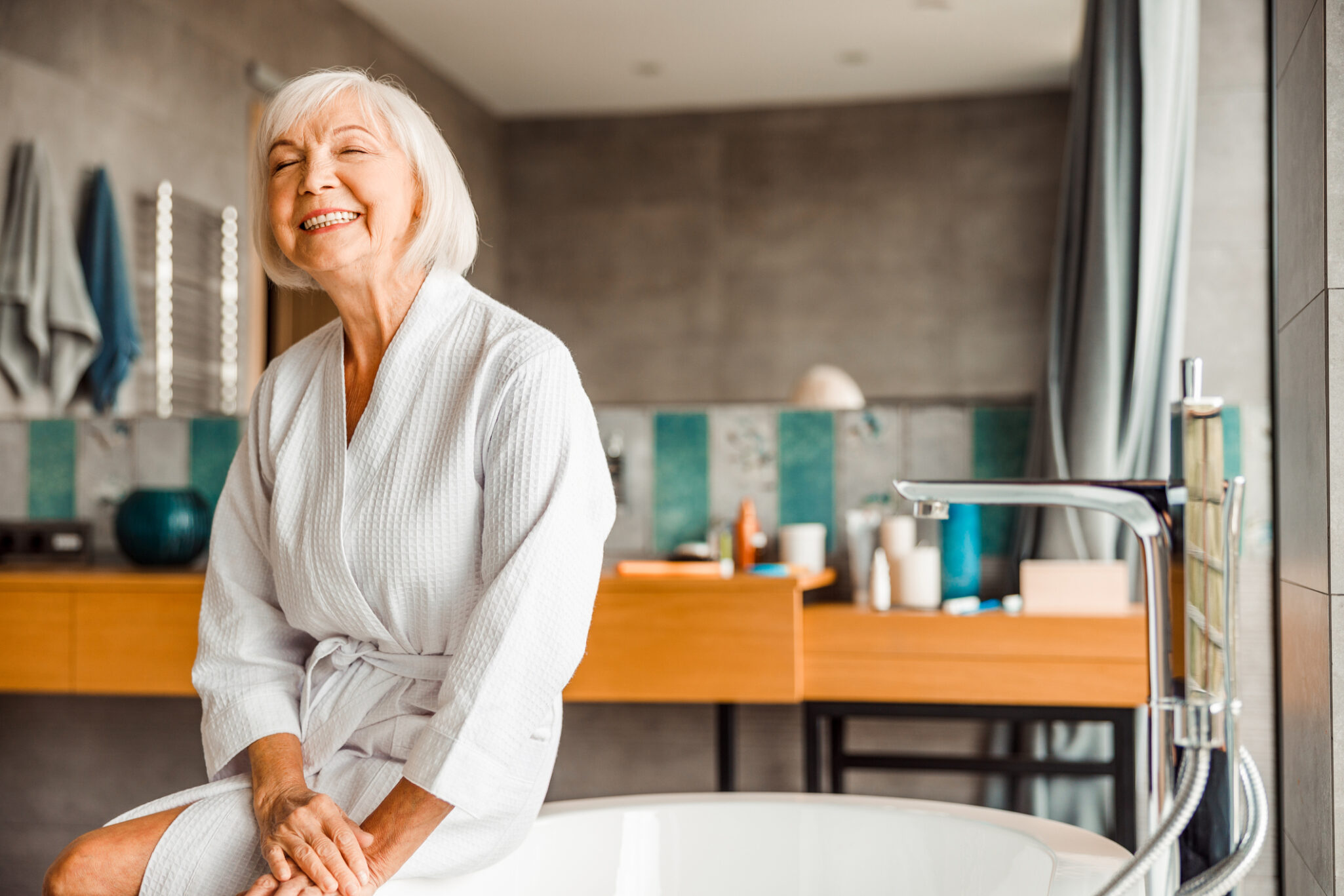 A senior woman in a white robe relaxing happily at a spa.