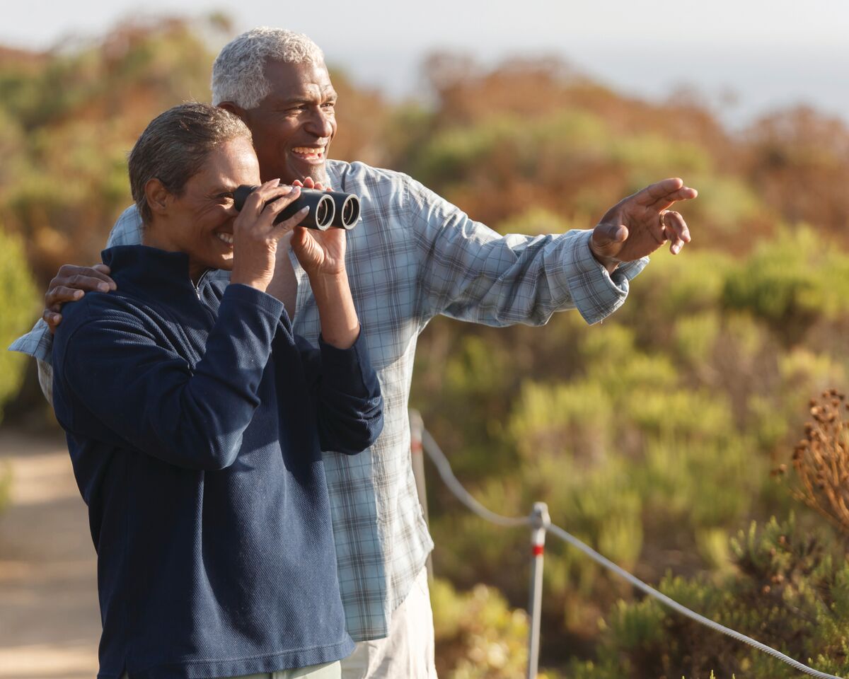 A senior couple use a pair of binoculars to bird watch.