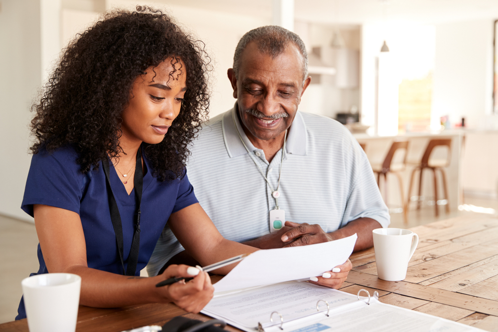 A senior man sits at a table with his home health nurse.