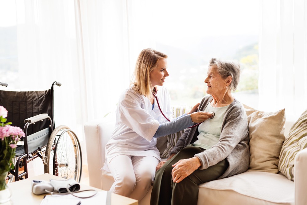 A home care provider examines a senior woman on a couch.