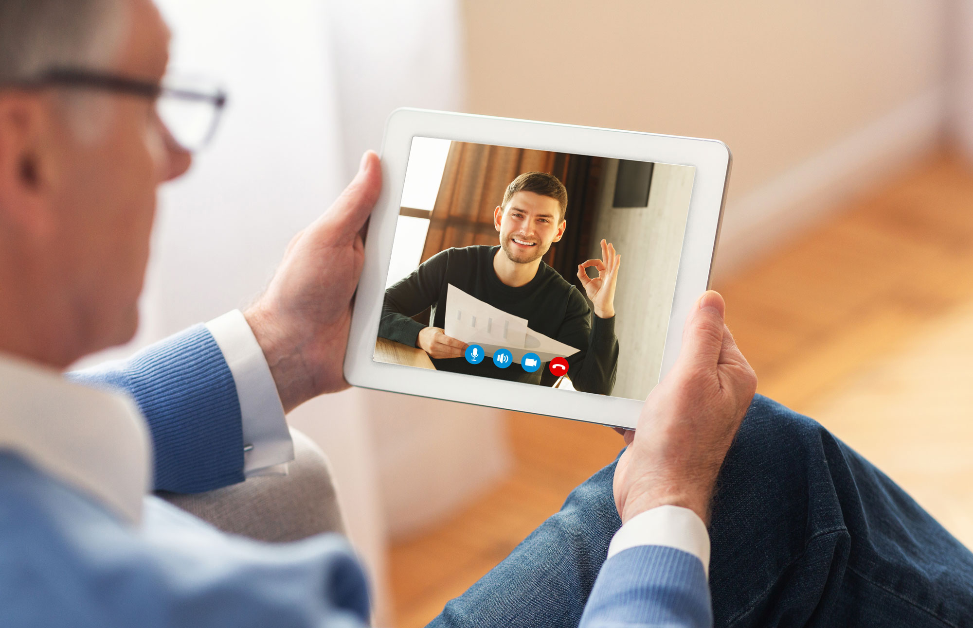 A senior man holding a tablet and talking on a video call.
