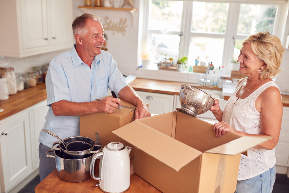 A senior couple pack kitchen items into moving boxes.