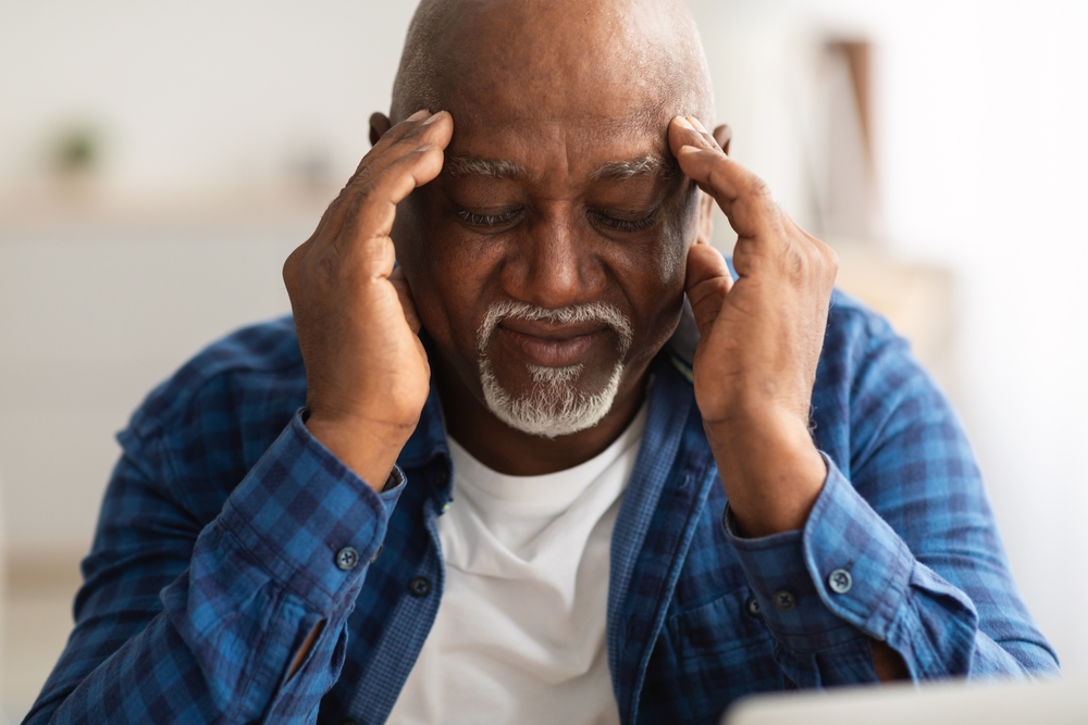 A senior man holds his head in his hands.