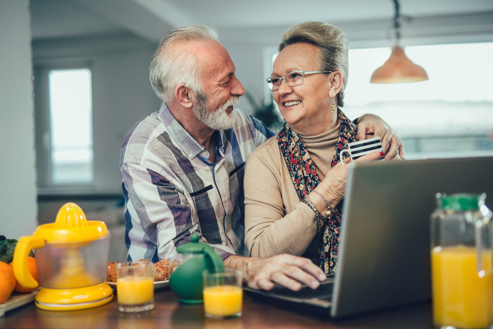 A senior man smiles with his arm around his wife.