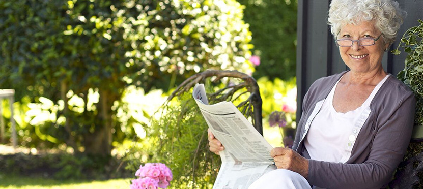 happy senior lady reading the newspaper on a bright sunny day