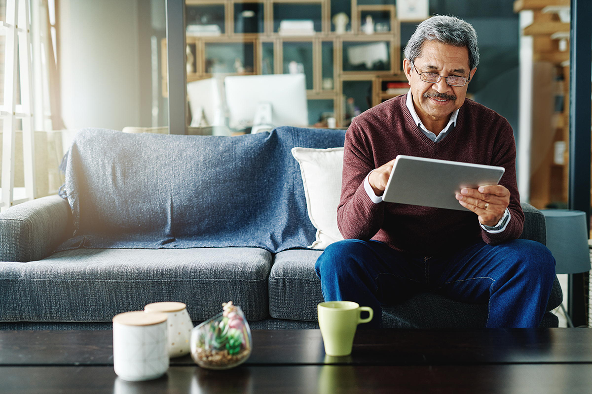 A senior man uses a tablet while sitting on a couch.