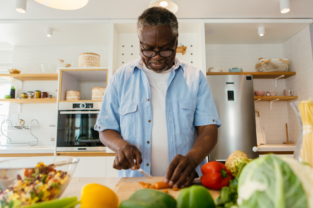 A senior man cuts up vegetables for a salad.