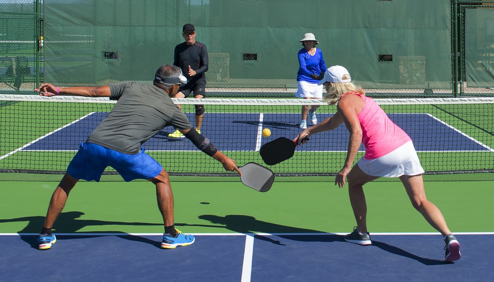 Two senior couples compete in a pickleball game.