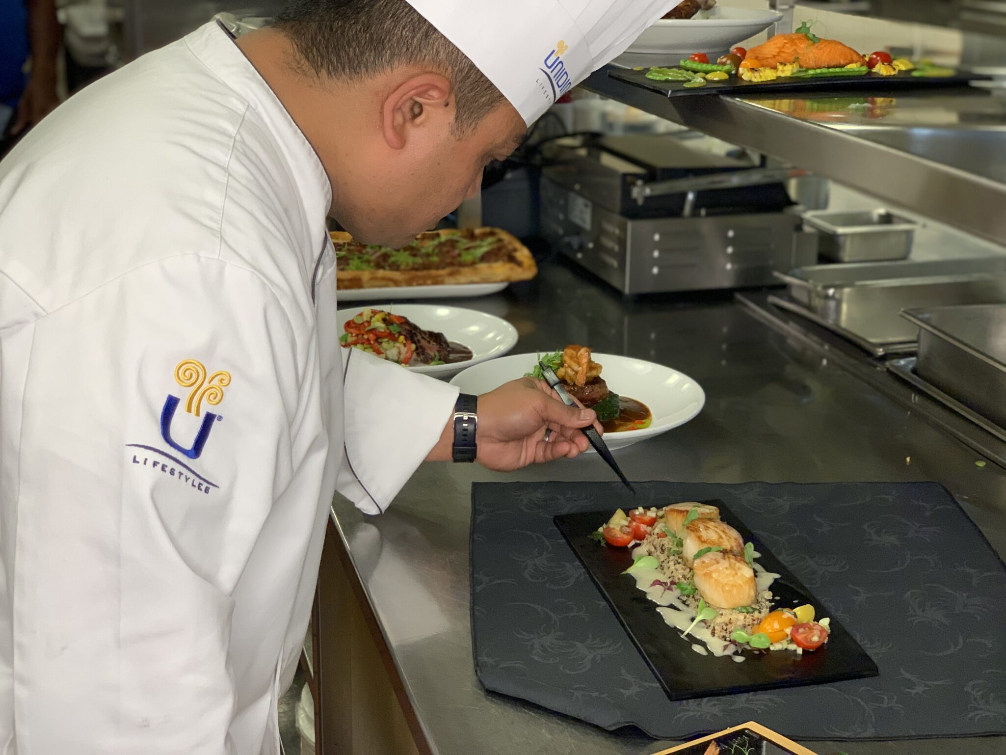 A chef carefully plates food on a black dish.