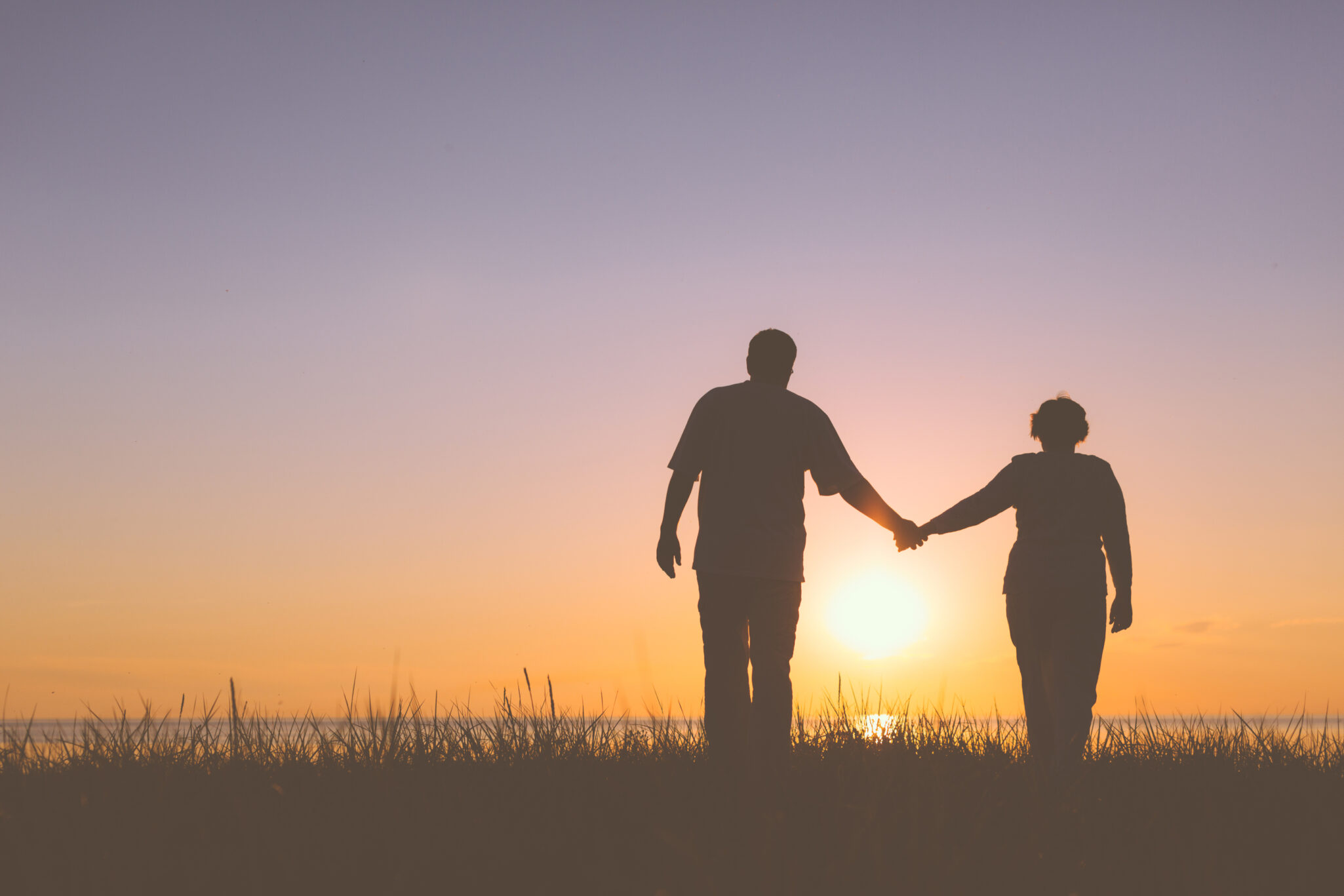 Silhouette of a senior couple holding hands and walking towards the ocean.