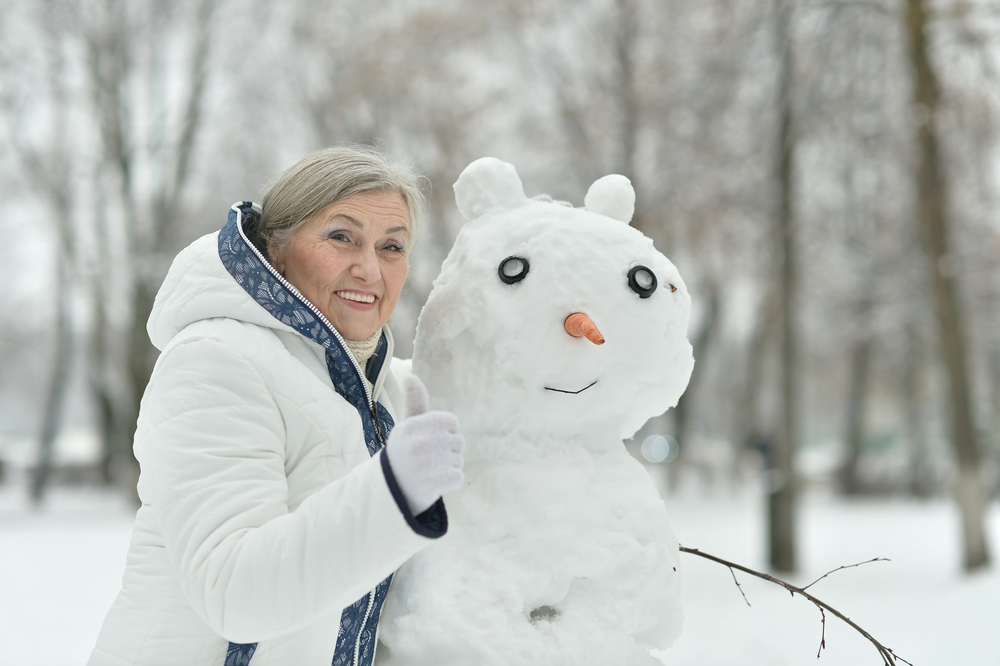 An older woman poses for a photo next to the snowman she built