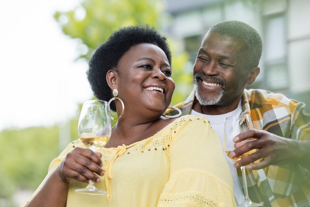 A senior woman and a senior man stand next to each other drinking white wine