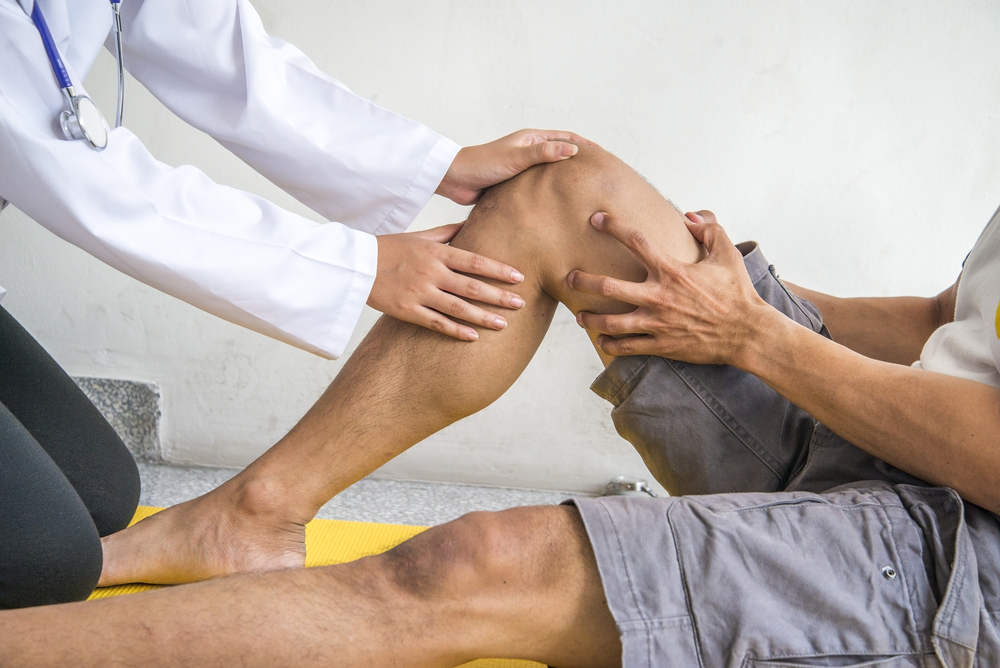 A health care worker examines a leg bent upwards and focuses on the knee joint movement