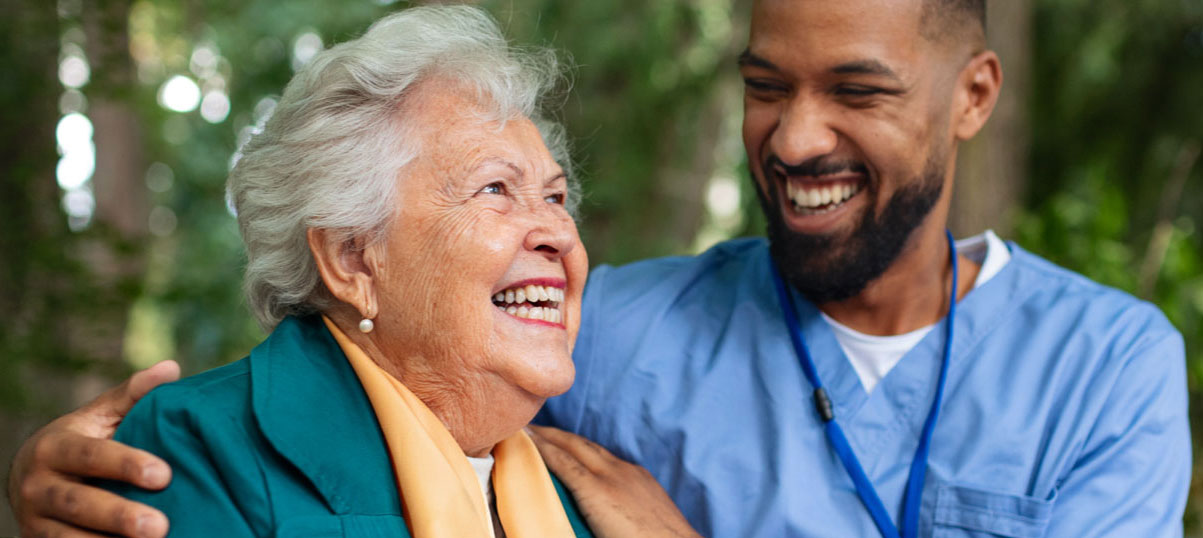 A senior woman and a male nurse laughing together.