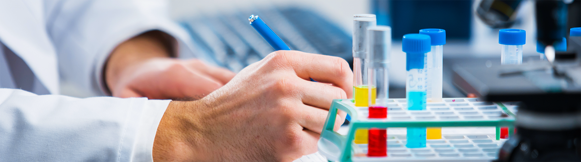 Close up of a scientist s hands taking notes next to colorful vials 