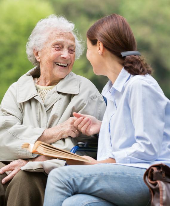 A senior woman and her care giver sit on a bench together