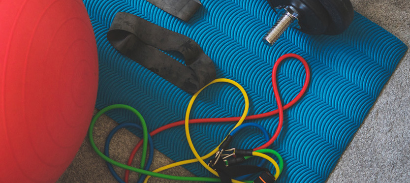 Close up of exercise bands and weights on a blue mat.